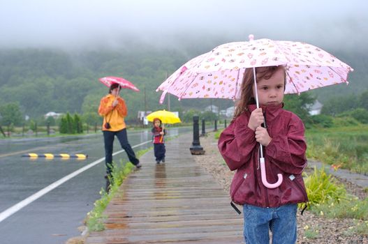 Family (mother, daughter and son) walking and playing under the rain with colorful umbrellas