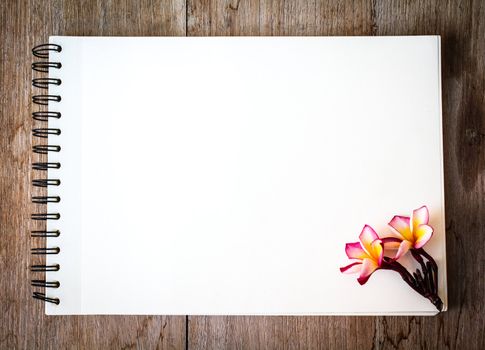 white notebook on the wood backgroung with pink flower