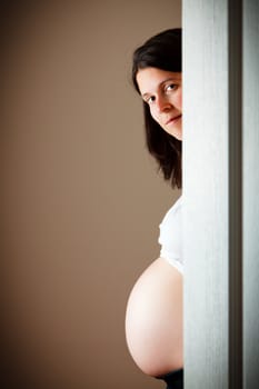 32 weeks pregnant woman hiding behind a door