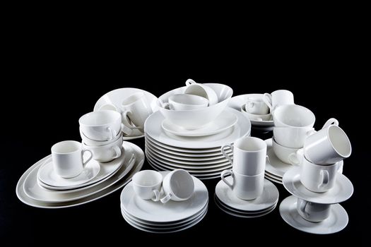 stack of mixed white dishes cups and plates isolated on black background