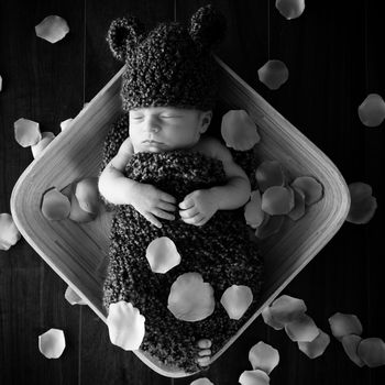 Newborn baby boy resting in a wool cocoon in a plate on a wooden floor