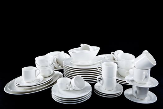 stack of mixed white dishes cups and plates isolated on black background