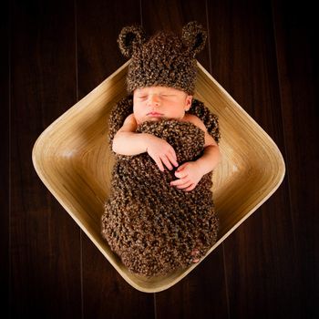 Newborn baby boy resting in a wool cocoon in a plate on a wooden floor