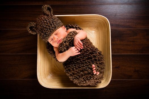 Newborn baby boy resting in a wool cocoon in a plate on a wooden floor