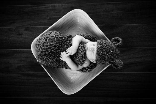 Newborn baby boy resting in a wool cocoon in a plate on a wooden floor