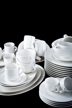 stack of mixed white dishes cups and plates isolated on black background