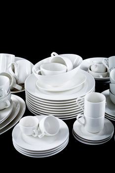 stack of mixed white dishes cups and plates isolated on black background