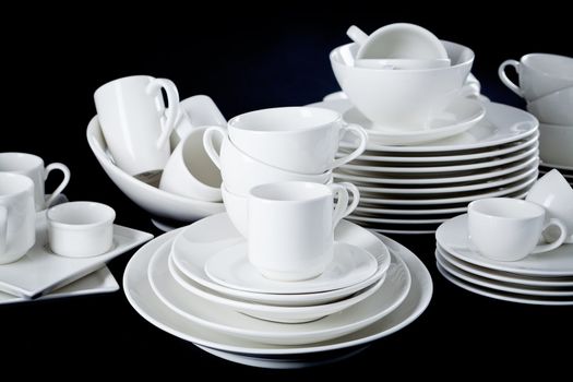stack of mixed white dishes cups and plates isolated on black background