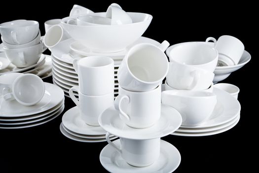stack of mixed white dishes cups and plates isolated on black background