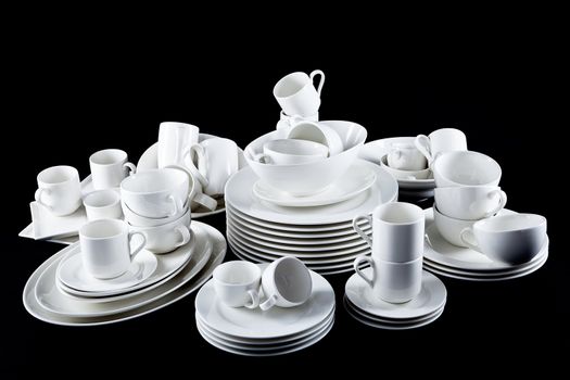 stack of mixed white dishes cups and plates isolated on black background
