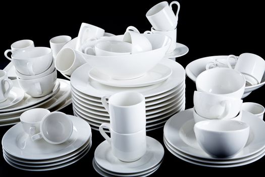 stack of mixed white dishes cups and plates isolated on black background