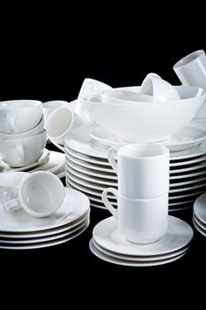 stack of mixed white dishes cups and plates isolated on black background