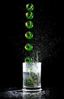Sequence of green ball falling into a water glash and splashes