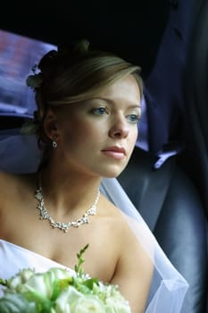 The beautiful bride with a bouquet in the automobile