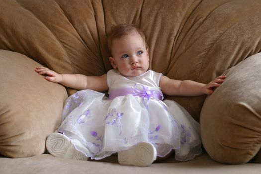 The little girl in a beautiful dress sits in the big armchair