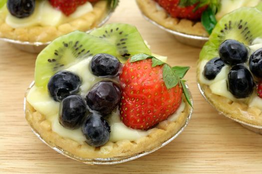 individual small fruit tart, filled with custard and decorated with a strawberry, blueberries and kiwi slices