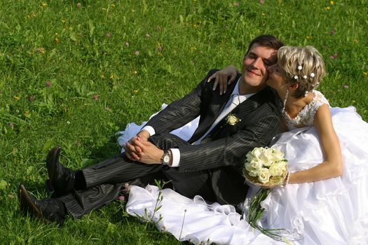 Beautiful newly-married couple sit on a grass