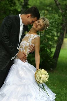 Groom gently embraces the bride in park