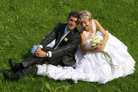 Beautiful newly-married couple sit on a grass