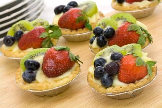 Six summer fruit tartlets on a wooden tray