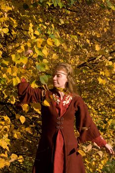 The blonde girl in medieval red dress in the autumn forest
