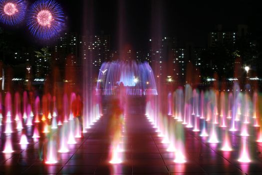 Series of colorful fountains at Night with children playing with fireworks in the background
