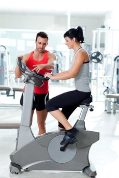 woman on stationary bicycle with personal trainer at fitness gym