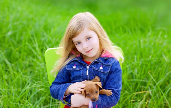 Blond kid girl with puppy pet dog sit in outdoor green grass