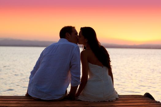 couple kissing at sunset sitting in jetty at orange sea lake