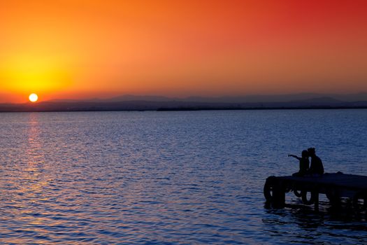 Mother and daughter in sunset jetty lake with orange sun