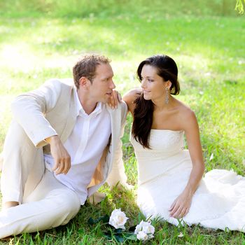 couple just married sitting in park green grass with white rose