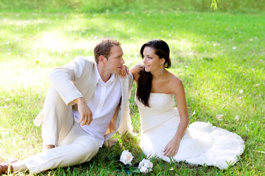 couple just married sitting in park green grass with white rose