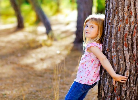 blond kid girl on autumn tree trunk in forest park