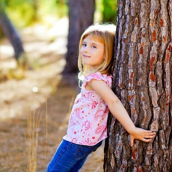 blond kid girl on autumn tree trunk in forest park