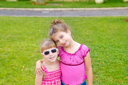 children girls hug in green grass park with pink dress