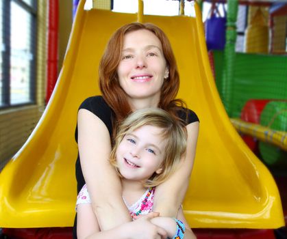 daughter and mother together in playground sitting on yellow slide