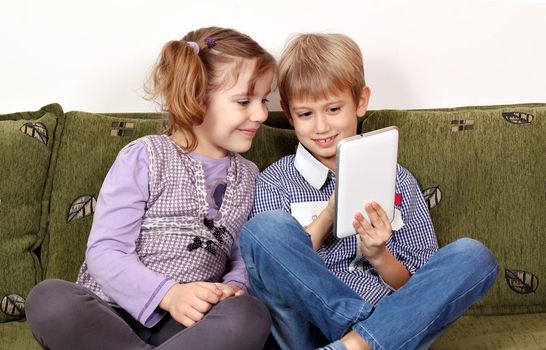 little girl and boy sitting on bed and play with tablet