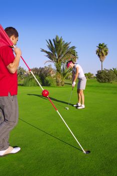 golf woman player putting golf ball and man holds flag