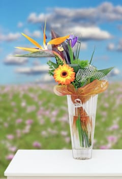 colorful floral arrangement in a vase on a white table - meadow with flowers in the background