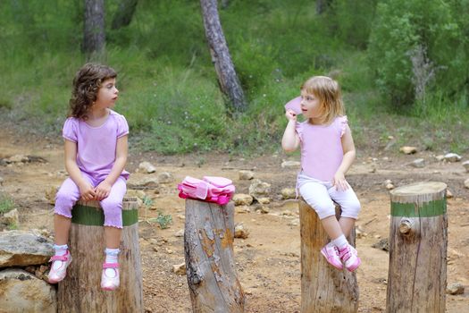 two little girls sit on forest park tree trunks green pine woods