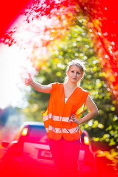 Young female driver wearing a high visibility vest on the roadside after her car has broken down