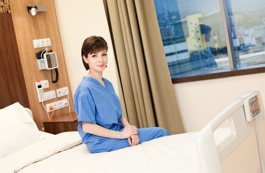 Positive female patient in blue gown sitting on hospital bed, looking at camera