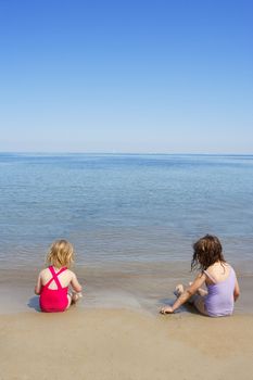 tow sisters sit on beach bathing suit swimsuit back view summer vacation