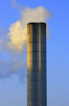 Large chimney sent clouds of steam into the blue sky