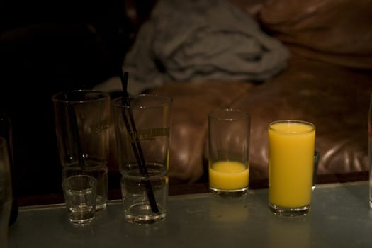 Glasses on a pub table, two glasses with orange juice and two empty glasses of alcohol next to each other, empty, full, cold drink, alcoholic, non alcoholic