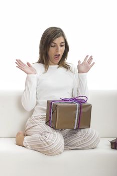 Woman in pajama seated on a sofa holding a Christmas gift