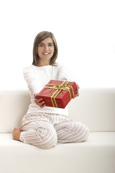 Woman in pajama seated on a sofa holding a Christmas gift