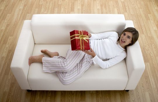 Woman in pajama seated on a sofa holding a Christmas gift