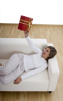 Woman in pajama seated on a sofa holding a Christmas gift