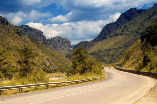 winding mountain road with car in the distance and cloudy sky